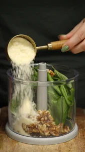 Parmesan added to basil, pine nuts and garlic in a food processor