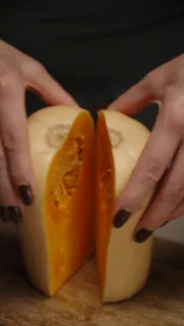 Hands scraping seeds from a small white pumpkin to prepare an edible soup bowl