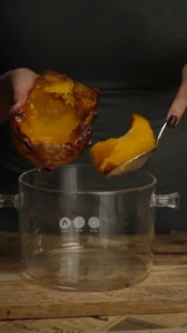 Roasted butternut squash flesh being scooped from its skin into a cooking pot