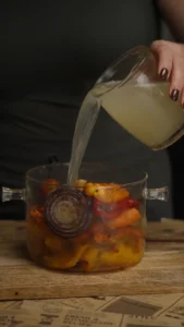 Vegetable broth being poured into a pot of roasted squash and vegetables