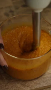 Orange butternut squash soup being blended until smooth with an immersion blender