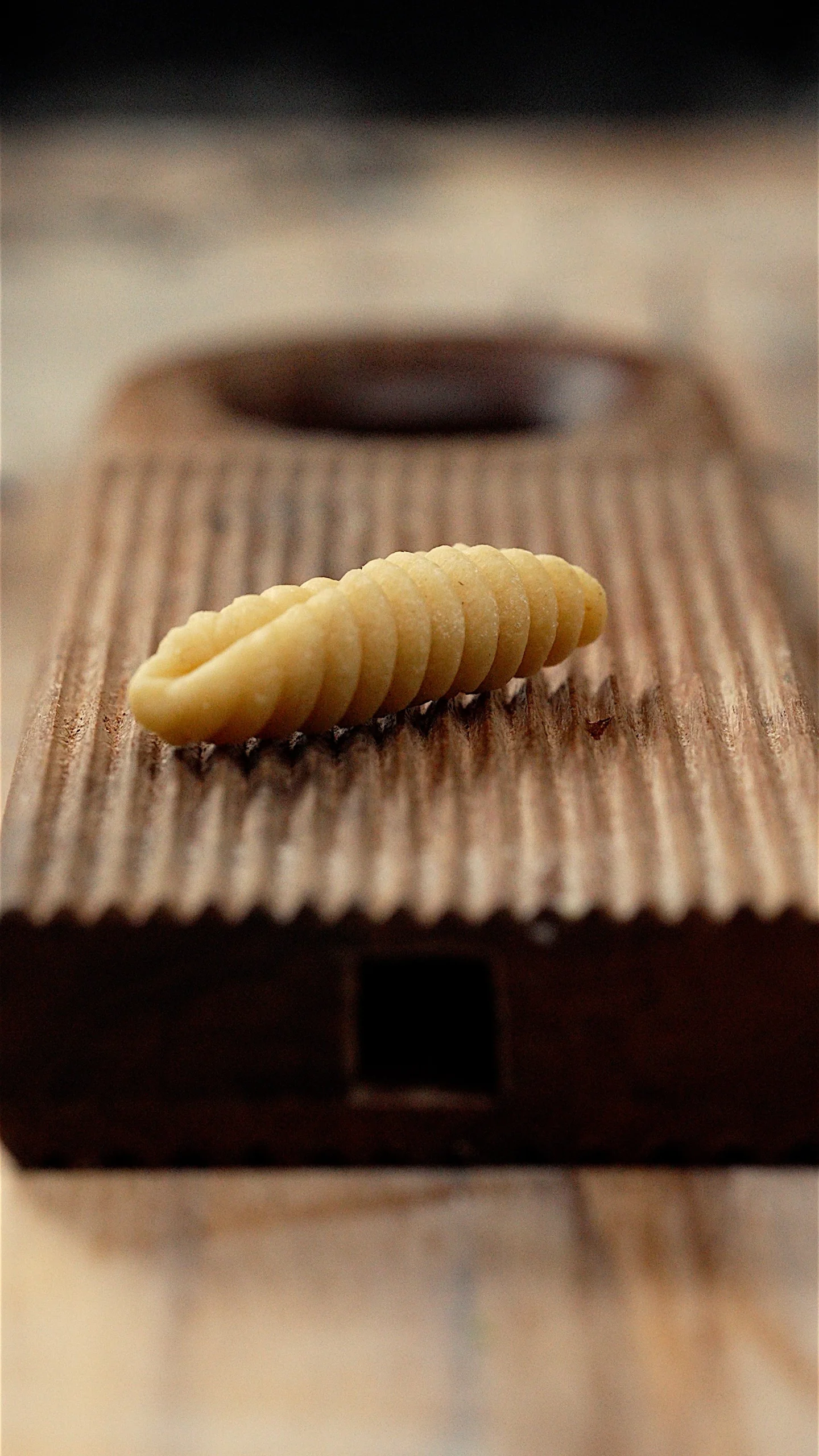 A piece of pasta being shaped on a wooden gnocchi board