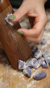 Purple potato gnocchi being shaped on a wooden gnocchi board